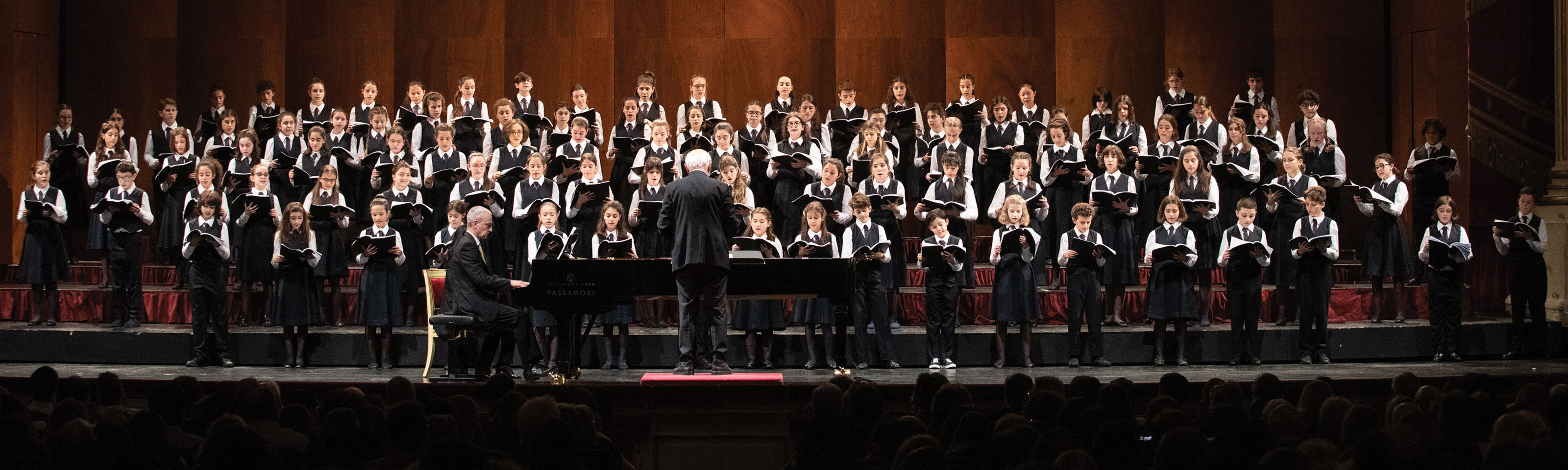 A children's choir in concert with conductor and piano accompanist